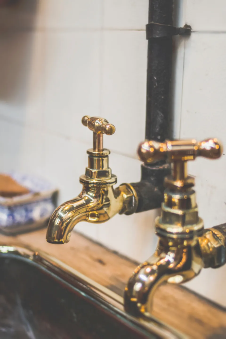 Pair of polished brass taps over a sink against white tiles