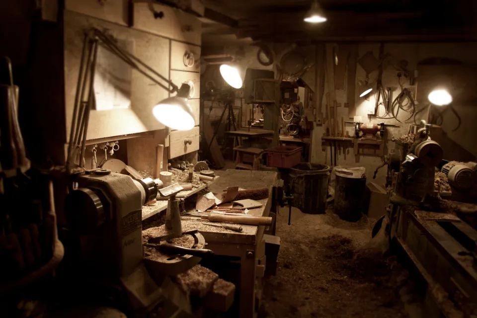 Workshop bench under lamplight, with hand tools on the wall