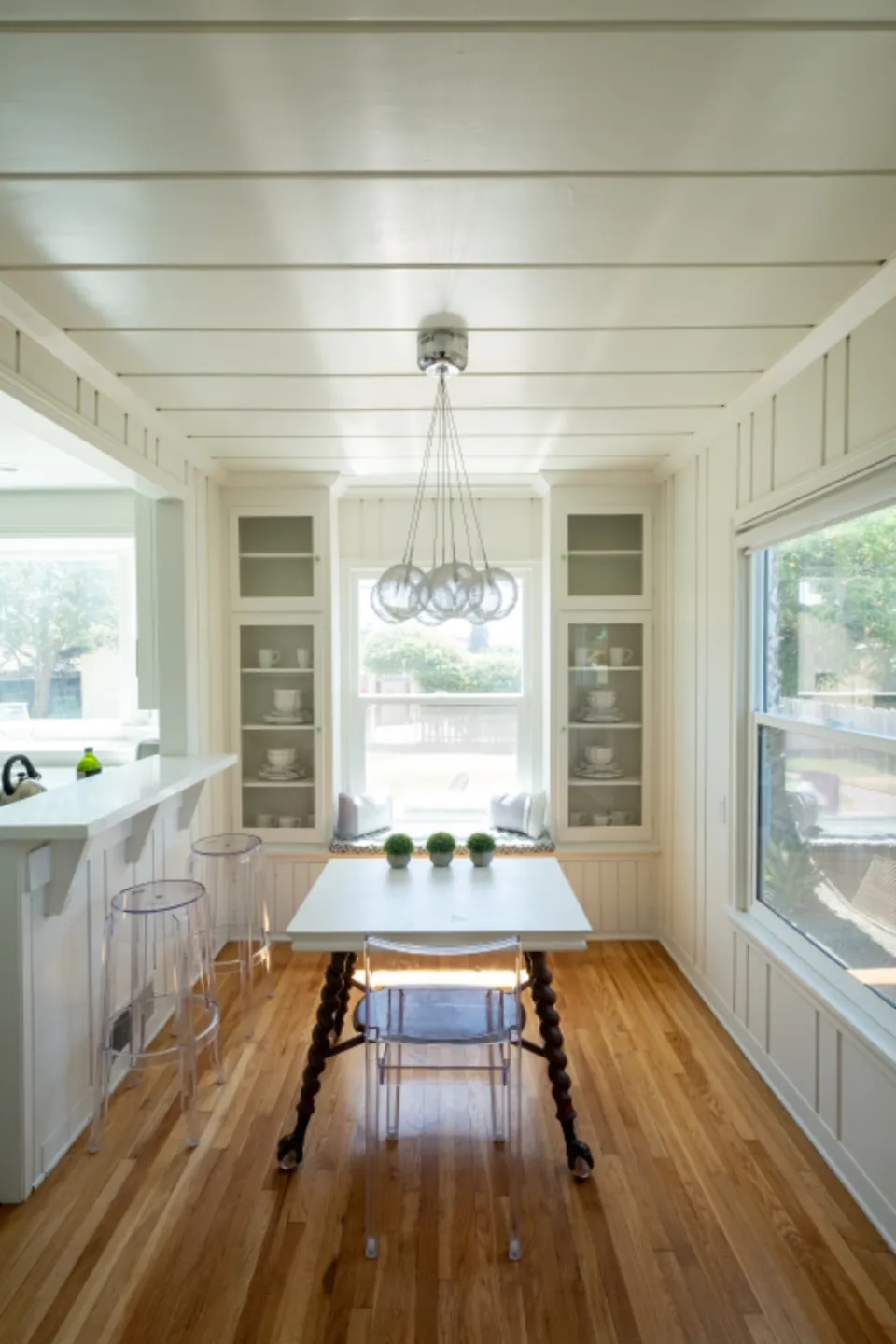 Narrow white kitchen with an island and a dining table under a pendant light
