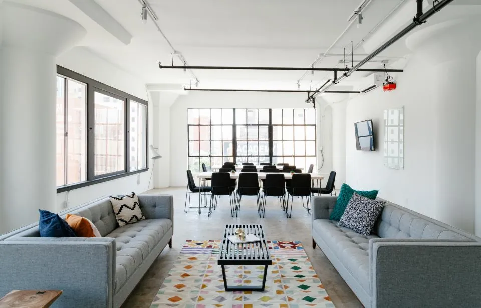 Open-plan loft with two grey sofas, a long dining table and steel-framed windows