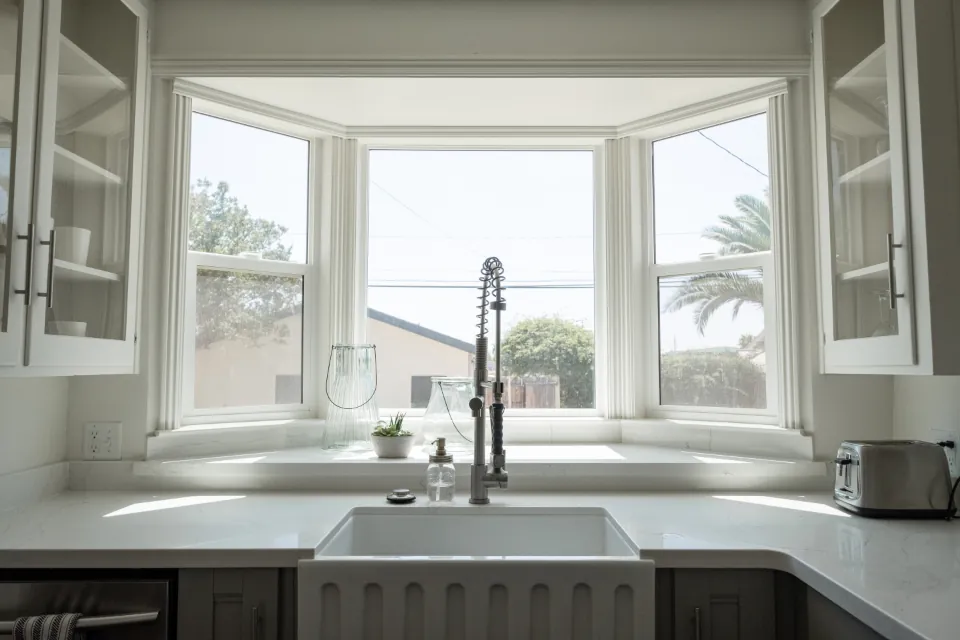 Kitchen with white cabinetry, a butler sink and a bay window over the worktop