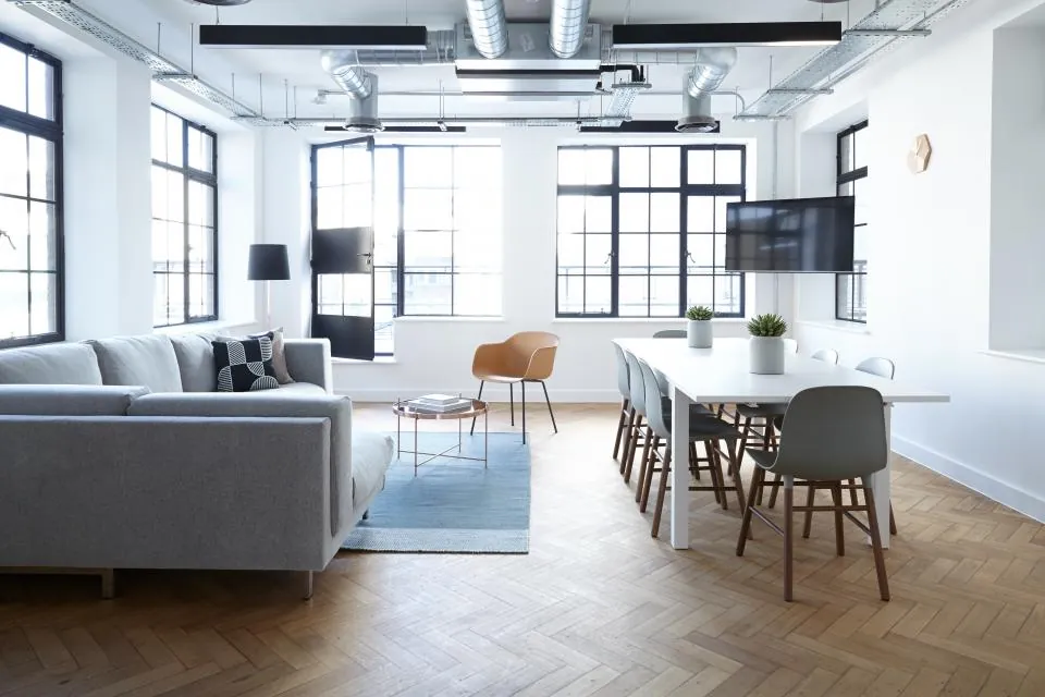 Warehouse loft with a long white work table, chairs and a grey sofa under steel-framed windows