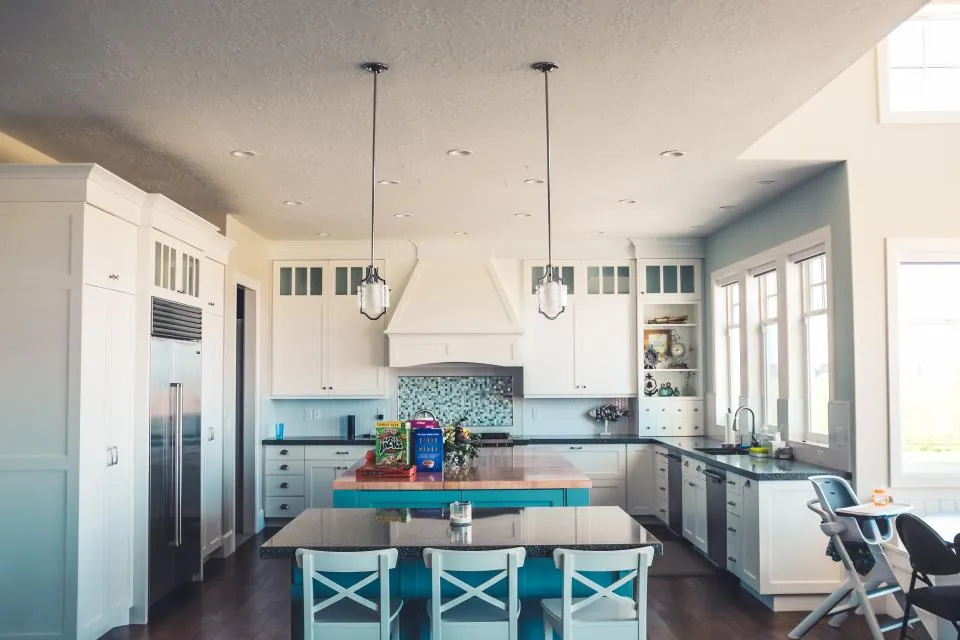 White kitchen with a central island, pendant lights and a dining table beyond